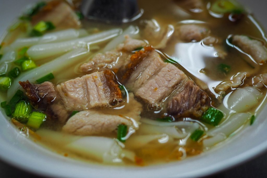 Steaming bowl of Kuay Jab Nam Sai with clear broth and rice noodles