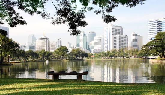 Green spaces in Bangkok – empty bench by the lake at Lumphini Park with city skyline view